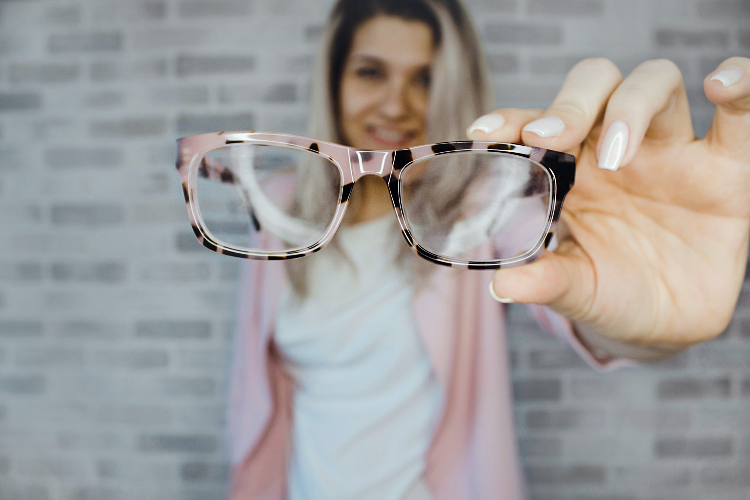 Pink eyewear being help up by a woman wearing pink and white. Learn what to do with your old eyewear.